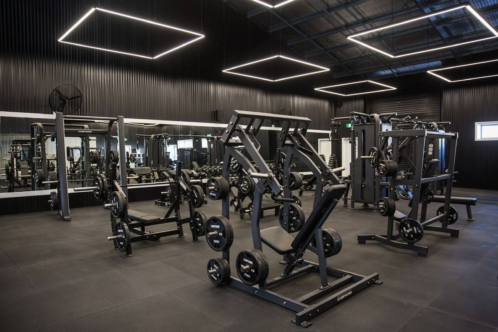 Plate-loaded machine zone under feature lighting in a 24/7 gym by Compound Fitness